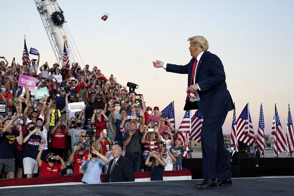 Presiden Donald Trump melemparkan masker ke arah para pendukungnya saat tiba di panggung untuk berkampanye di Bandara Internasional Orlando Sandford, Florida, AS, Senin (12/10/2020). 