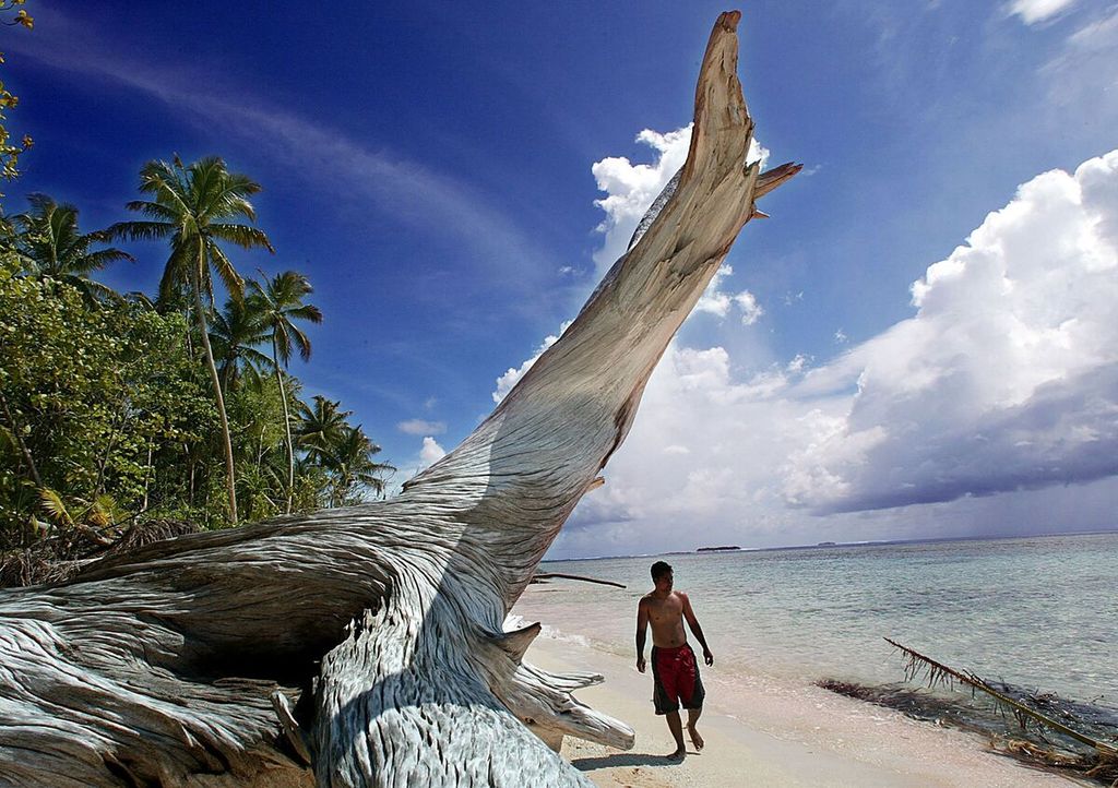 Seorang pria berjalan melewati sepotong kayu apung raksasa di bibir pantai Pulau Tepuka di Atol Funafuti. Foto diambil pada 22 Februari 2004.
