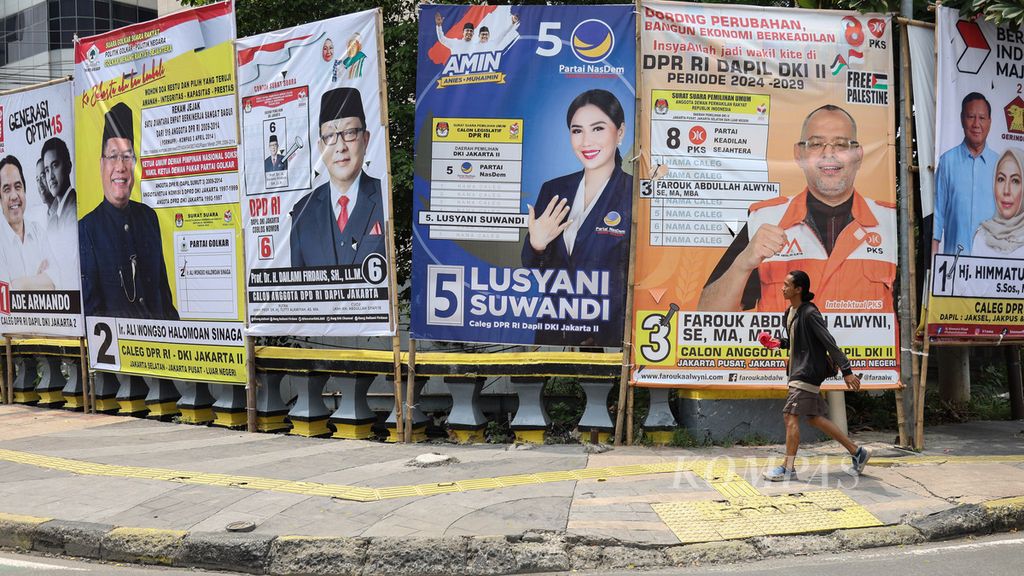 Seorang pemuda berjalan di samping baliho peserta Pemilu 2024 di Jalan Abdul Muis, Jakarta, Selasa (5/12/2023).