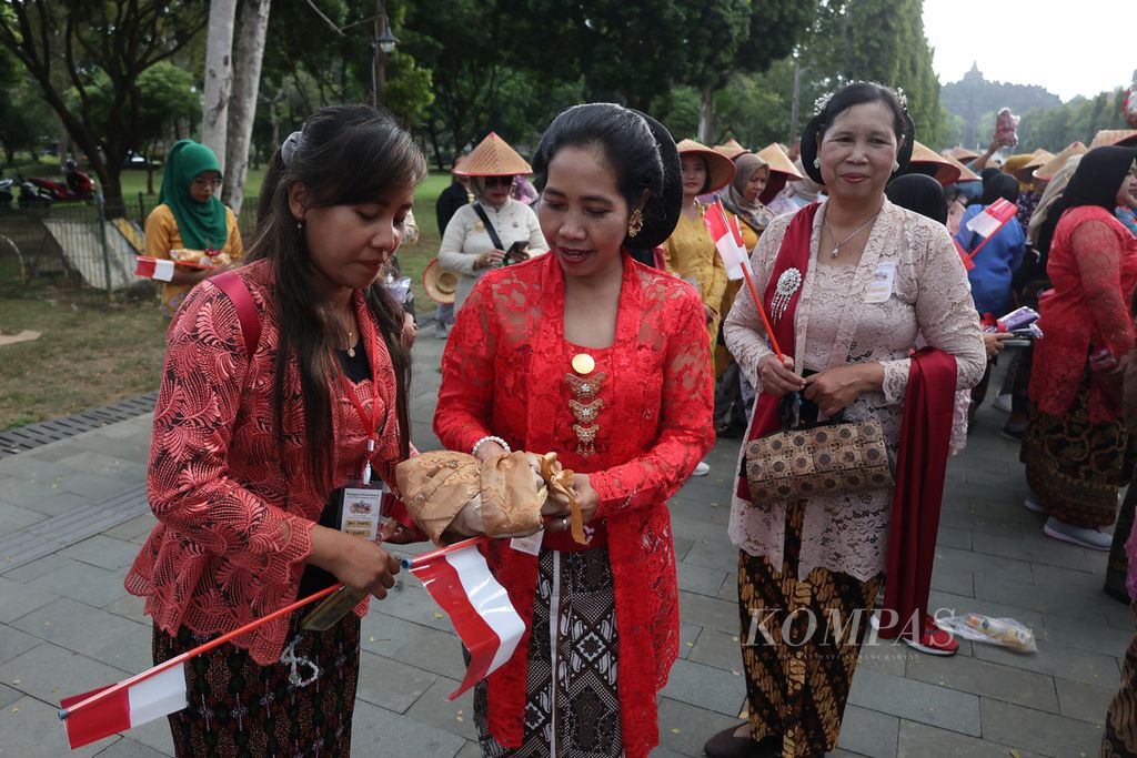 Perempuan berkebaya memberikan baju kebaya kepada pedagang kawasan Borobudur sebagai wujud semangat berbagi saat mengikuti acara peringatan Hari Kebaya Nasional di kawasan Concourse Candi Borobudur, Magelang, Jawa Tengah, Rabu (24/7/2024). 