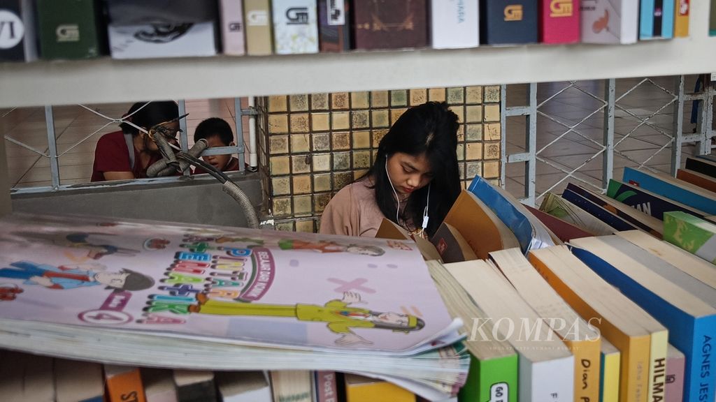 Wulandini (22), warga Mangga Dua, Jakarta Pusat, meluangkan waktu liburnya untuk membaca buku di perpustakaan mini Gramedia Stasiun Jakarta Kota, Sabtu (2/3/2024).