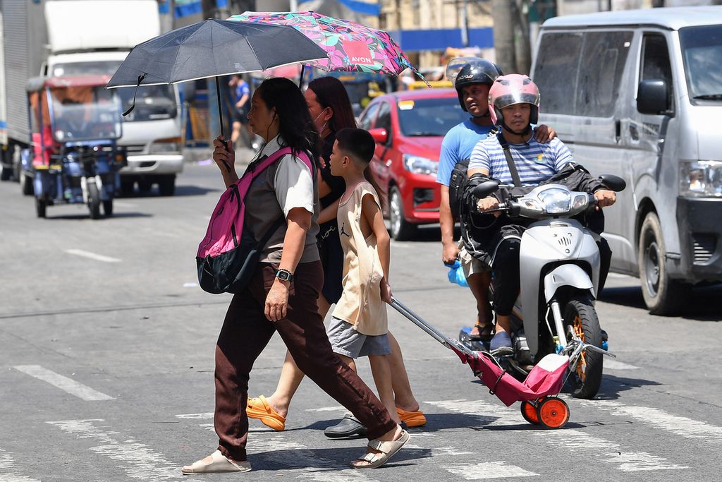 Pejalan kaki menggunakan payung untuk melindungi kepalanya dari sengatan terik matahari saat berjalan di Manila, Filipina, 25 April 2024. 