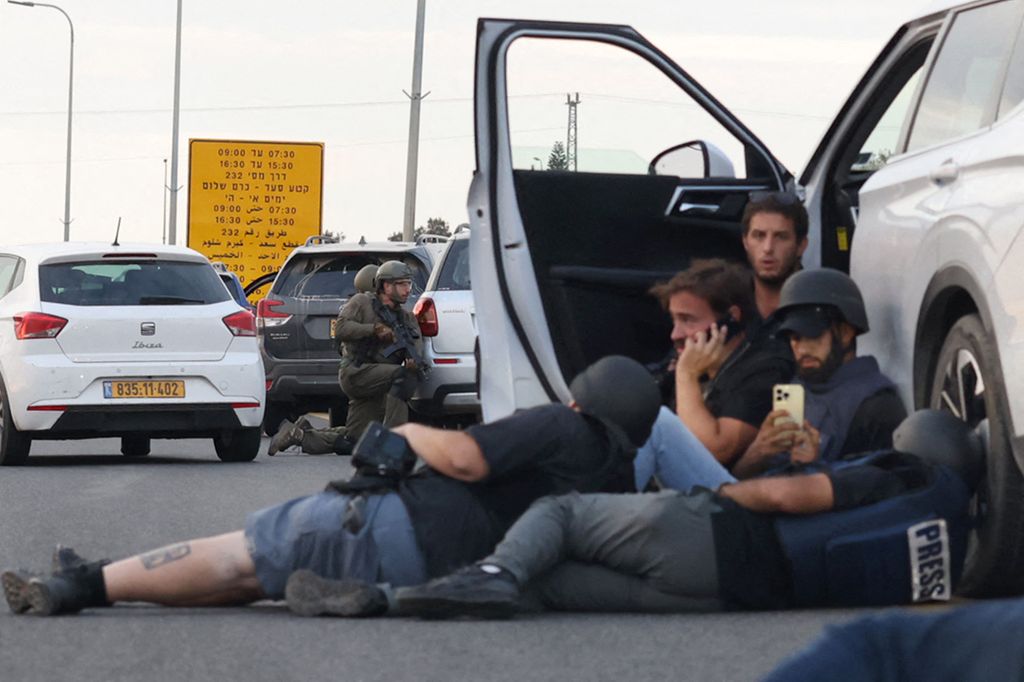 Jurnalis berlindung di balik mobil ketika tentara Israel mengambil posisi selama bentrokan dengan pejuang Palestina di dekat Gevim Kibbutz, dekat perbatasan dengan Gaza, Sabtu (7/10/2023). 