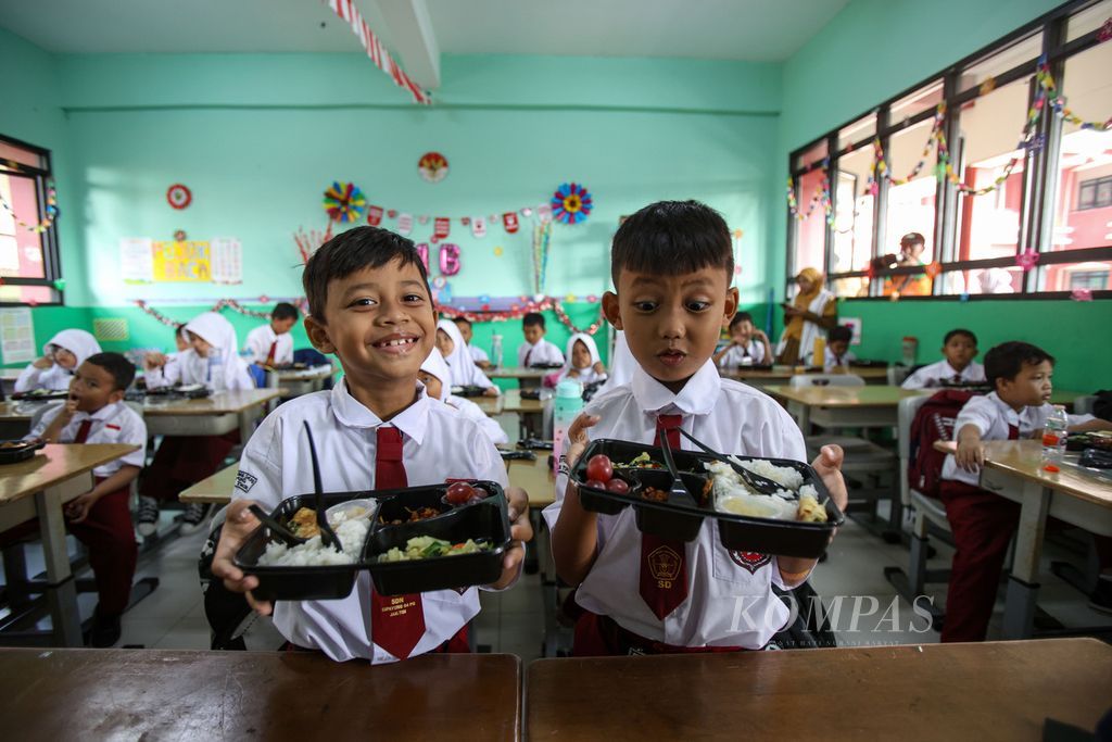 Dua siswa memperlihatkan paket makanan makan bergizi gratis di SDN 04 Cipayung, Jakarta Timur, Senin (26/8/2024). Pemerintah Provinsi DKI Jakarta kembali menggelar uji coba program makan bergizi gratis. 