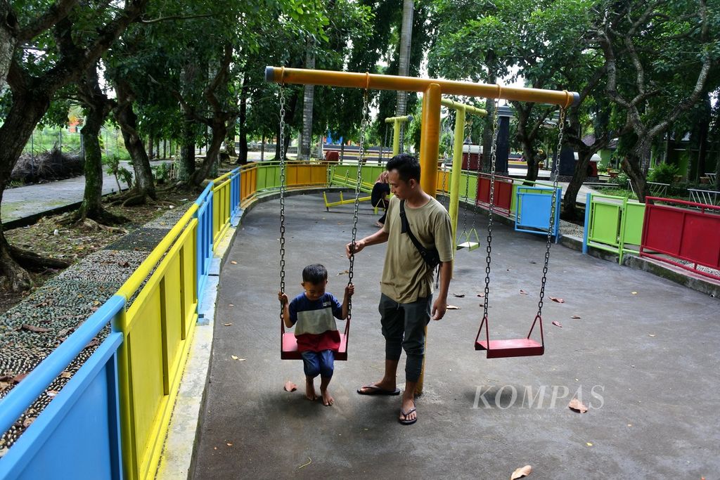 Roni Irawan (28) menemani putranya, Respan (4,5), mencoba fasilitas bermain anak di kawasan Ruang Terbuka Hijau Taman Selagalas, Mataram, Nusa Tenggara Barat, Senin (15/1/2024). 