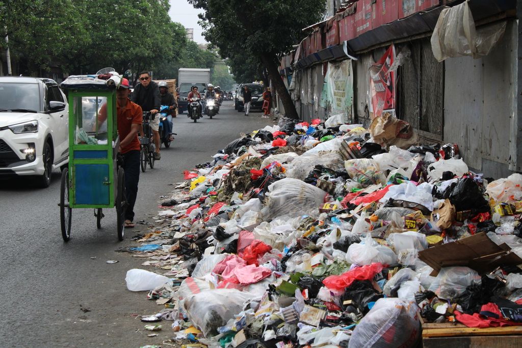 Salah satu pedagang keliling melewati tumpukan sampah di sisi Jalan Ahmad Yani di dekat Pasar Cicadas, Kota Bandung, Jawa Barat, Minggu (5/11/2023). 