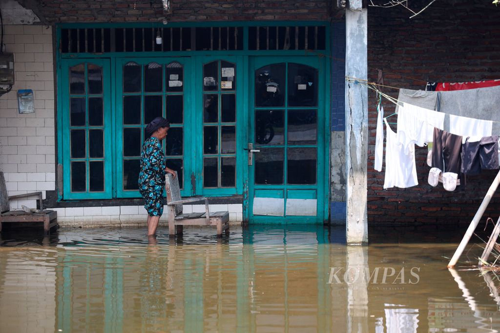 Warga di depan rumahnya yang masih tergenang banjir di Desa Kalisari, Kecamatan Sayung, Kabupaten Demak, Jawa Tengah, Selasa (10/1/2023).