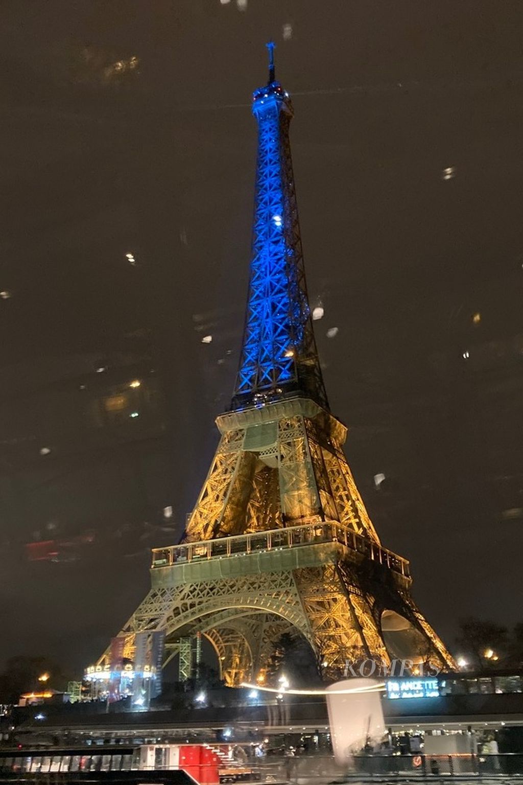 Menara Eiffel disorot lampu dengan warna bendera Ukraina untuk memperingati satu tahun invasi Rusia atas negara itu pada Kamis (23/2/2023) malam. Foto diambil dari balik kaca jendela Bateau Parisien, perahu wisata yang melintasi Sungai Seine di tengah kota Paris, Perancis. 