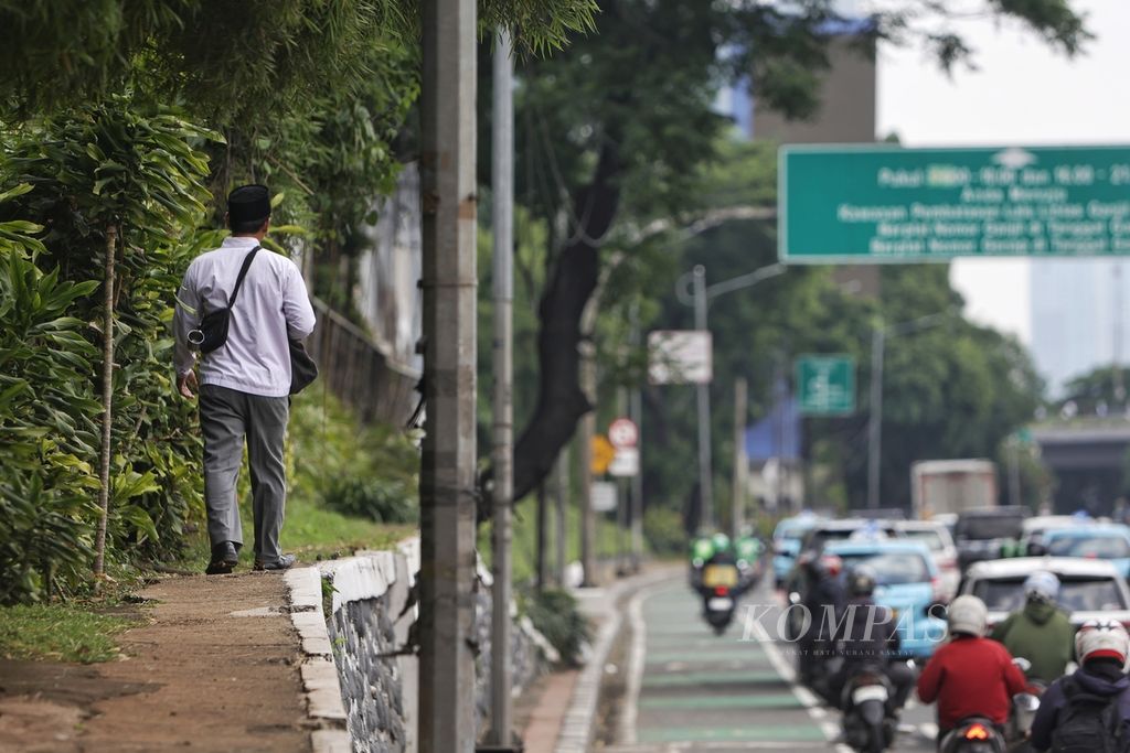 Pejalan kaki melintasi trotoar yang menanjak dan dipenuhi tanaman di Jalan Gatot Subroto, Jakarta, Jumat (1/3/2024). Meski proyek revitalisasi trotoar terus digiatkan, kondisi trotoar di sejumlah wilayah di Jakarta masih menyulitkan pejalan kaki untuk melintas. 