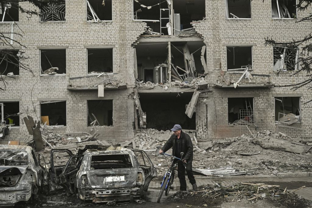 Seorang pria dengan sepedanya berada di depan sebuah bangunan yang hancur setelah serangan di kota Sloviansk, Ukraina, pada 27 Maret 2023.  
