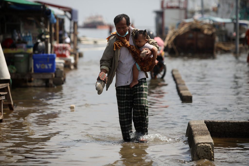 Seorang bapak menggendong anaknya saat melintasi kawasan dermaga Pelabuhan Kaliadem, Muara Angke, Jakarta Utara, yang tergenang banjir rob akibat air pasang, Rabu (21/10/2020).