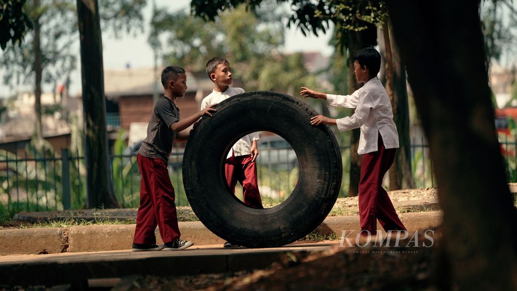 Pelajar sekolah dasar bermain ban truk sepulang sekolah di Kanal Timur, Duren Sawit, Jakarta Timur, Jumat (13/5/2022). 