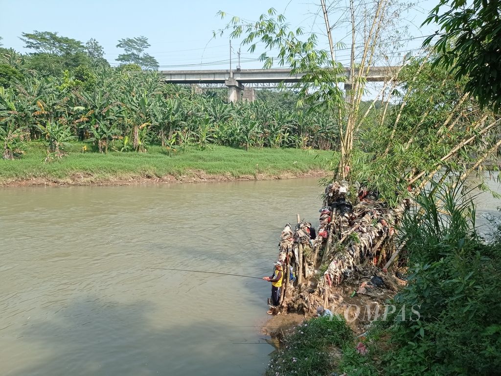 Pemancing dengan tumpukan sampah di sampingnya di Sungai Cisadane di kawasan Serpong, Tangerang Selatan, Banten, Sabtu (9/10/2021).