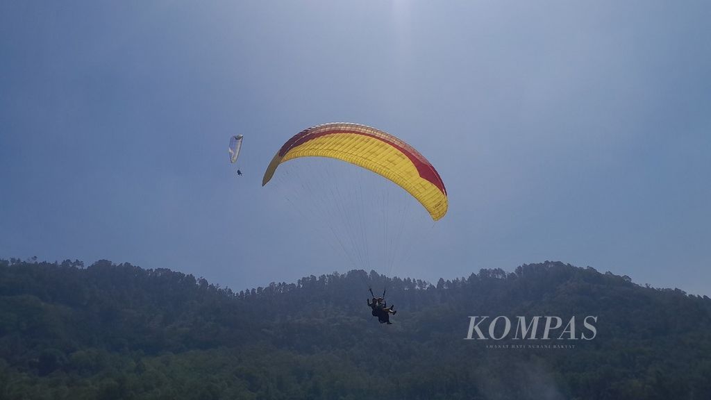Dua parasut yang digunakan terbang tandem oleh wisatawan asal Singapura tengah melayang di atas lokasi pendaratan paralayang Gunung Banyak di Lapangan Songgo Maruto, Songgokerto, Kota Batu, Jawa Timur, Rabu (9/8/2023).