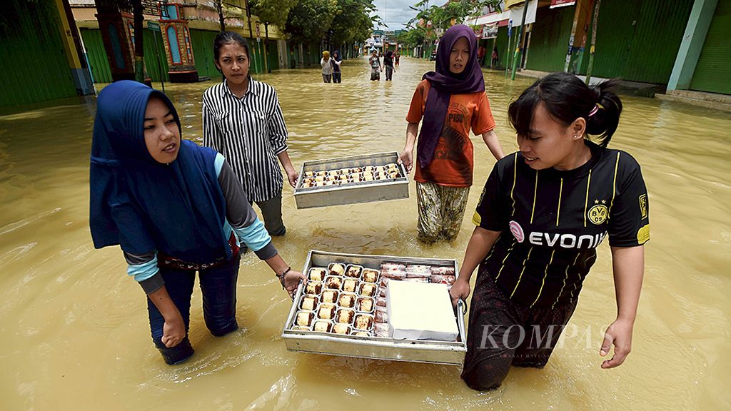 Warga melintasi banjir sambil membawa kue untuk dijual di Jalan Panglima Sudirman, Kabupaten Sampang, Jawa Timur, Senin (12/3). Banjir di kawasan itu akibat Sungai  Kemuning tidak mampu menampung curah hujan yang tinggi sehingga menggenangi wilayah sekitarnya.