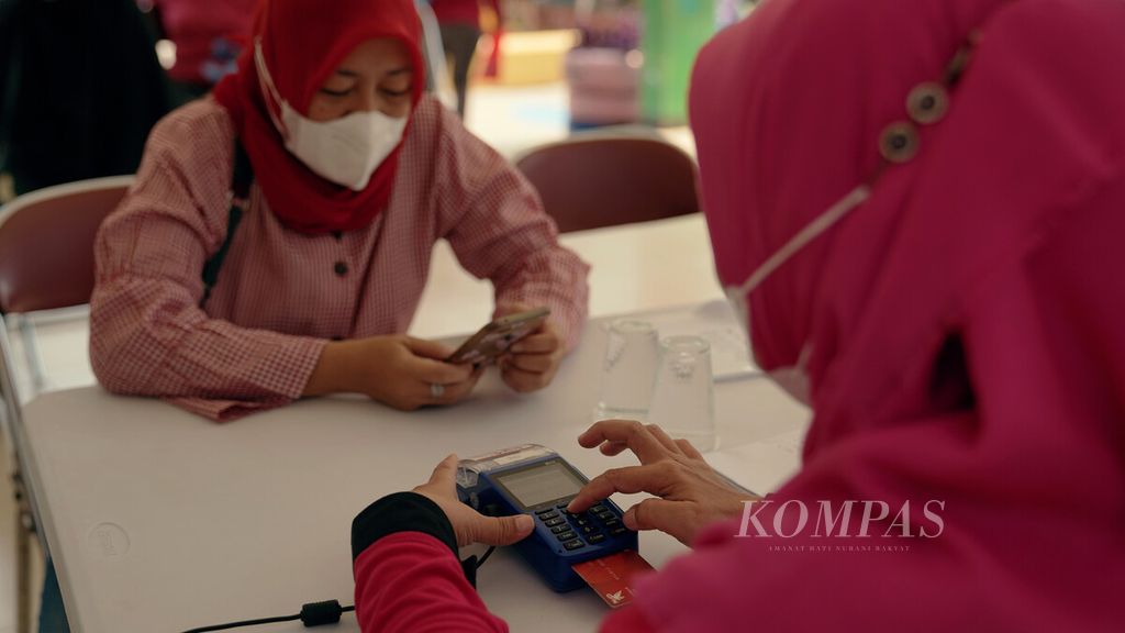 Petugas menggesek kartu menjelang pendistribusian pangan bersubsidi di Ruang Publik Terpadu Ramah Anak (RPTRA) Manunggal Juang, Kelurahan Sukapura, Kecamatan Cilincing, Jakarta Utara, Senin (14/3/2022). 