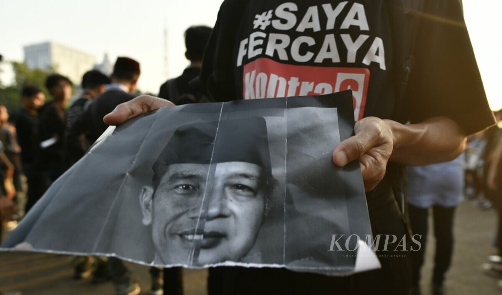 Peserta membawa poster yang menampilkan wajah Presiden Joko Widodo dan Presiden kedua Soeharto saat mengikuti Aksi Kamisan ke-589 di seberang Istana Merdeka, Jakarta, Kamis (20/6/2019). 