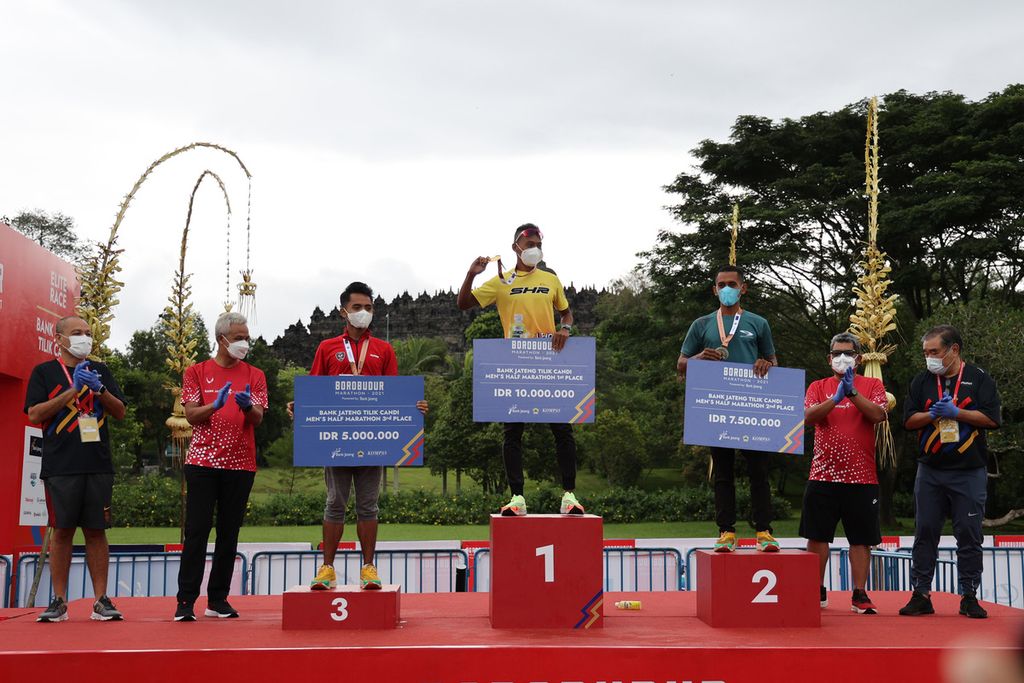 Pelari Irmansah (tengah) menjuarai lomba lari Bank Jateng Tilik Candi di kompleks Candi Borobudur, Magelang, Jawa Tengah, Minggu (28/11/2021) pagi. Irmansah tampil sebagai juara pertama dengan catatan waktu 1 jam 15 menit 58 detik. Juara kedua diraih oleh Muhsen (ketiga dari kanan) dengan catatan waktu 1 jam 22 menit 2 detik sedangkan juara ketiga diraih oleh Taufiq Narendra Purnama (ketiga dari kiri) dengan catatan waktu 1 jam 22 menit 25 detik. Pemberian hadiah dilakukan oleh Gubernur Jawa Tengah Ganjar Pranowo (kedua dari kiri) dengan disaksikan oleh CEO Kompas Gramedia Liliek Oetama (kiri), Ketua Yayasan Borobudur Marathon Liem Chi An (kanan) dan Direktur Keuangan Bank Jateng Dwi Agus Pramudya (kedua dari kanan).