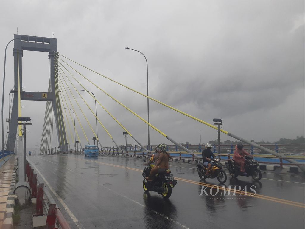 Pengendara sepeda motor menembus hujan di Jembatan Soekarno, Manado, Sulawesi Utara, Senin (18/1/2021). Cuaca buruk akibat La Nina berpuncak pada gelombang dan ombak besar yang menerjang Teluk Manado sehingga menyebabkan kerusakan parah di kawasan bisnis yang dibangun di atas lahan reklamasi.