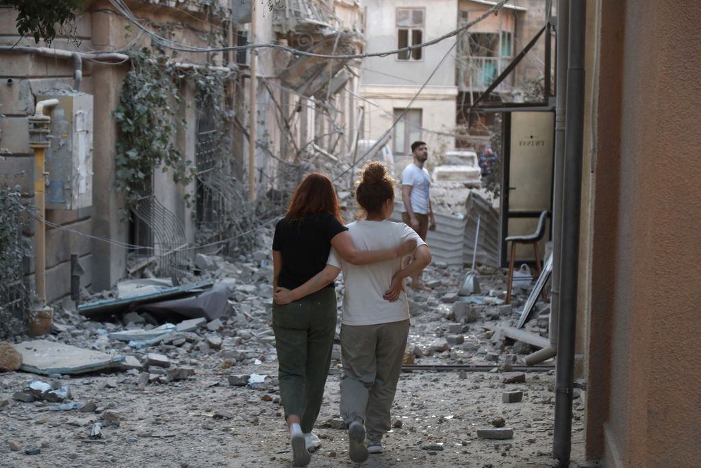Penduduk lokal berjalan bergandengan di antara puing-puing bangunan yang rusak akibat serangan rudal Rusia di Odesa, Ukraina, Minggu (23/7/2023).