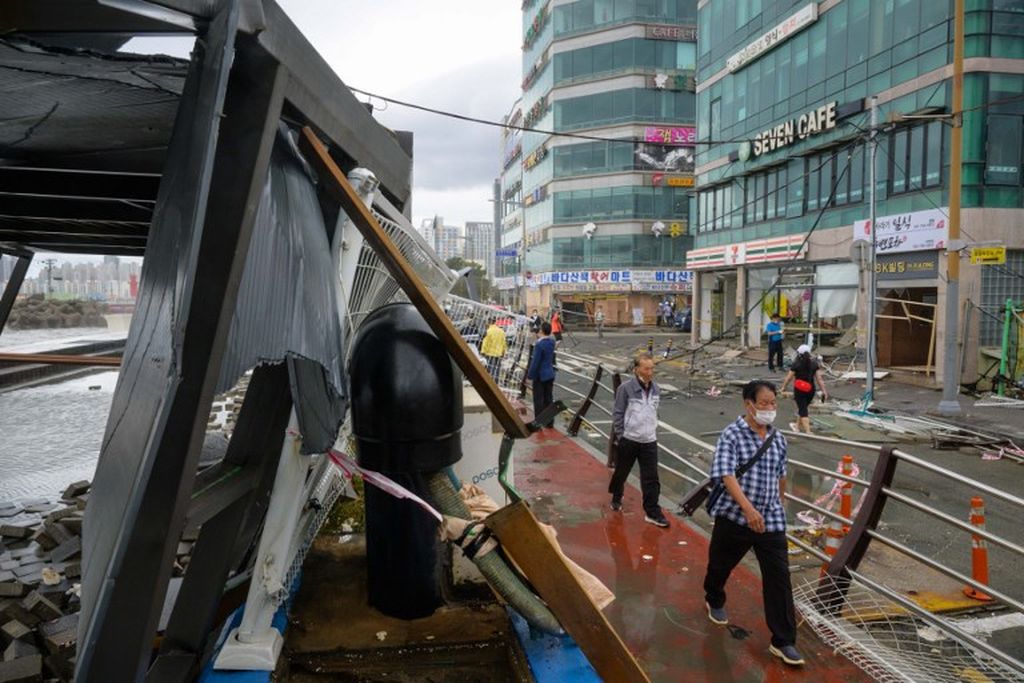 Para pejalan kaki melintasi struktur bangunan yang rusak akibat diterjang topan Hinnamnor di Busan, 6 September 2022.  