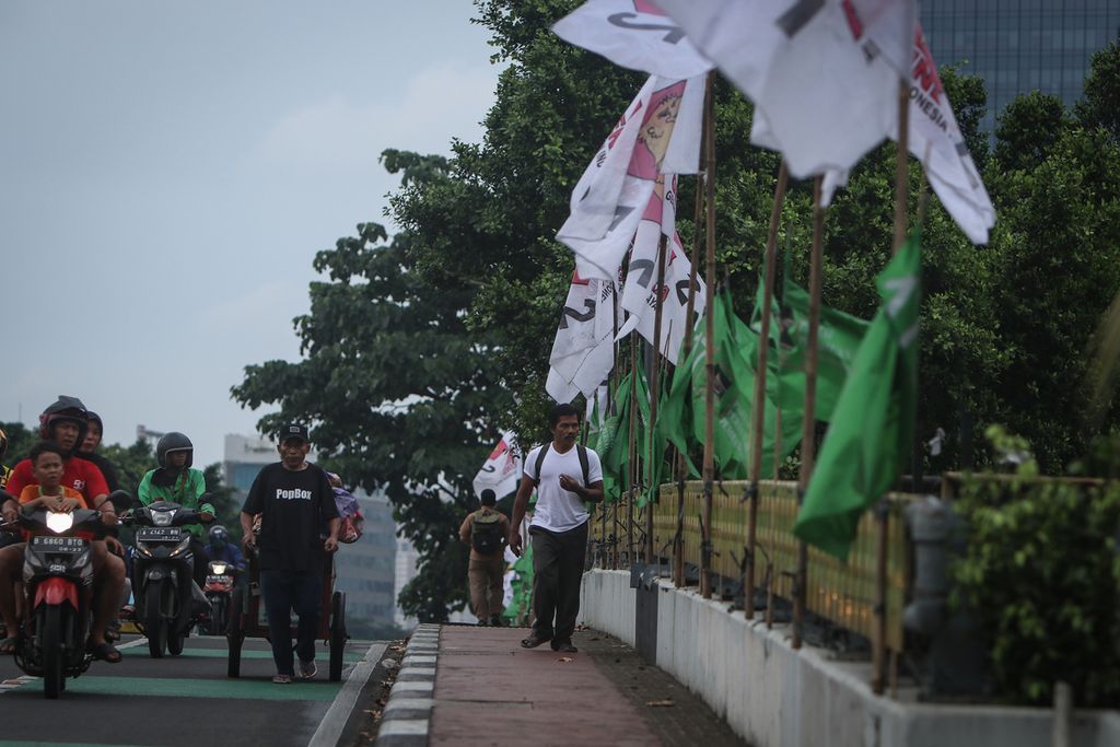 Warga melintas di samping bendera partai politik yang terpasang pada pembatas jembatan di Jalan Gatot Subroto, Jakarta, Selasa (7/2/2023). Sejumlah partai politik mulai memasang bendera dan spanduk untuk menarik perhatian calon pemilih. Sebelumnya, KPU telah menetapkan 18 partai sebagai peserta Pemilu 2024. 