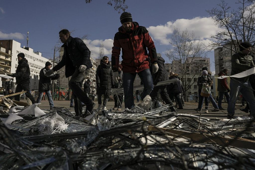 Warga membersihkan puing-puing di luar pusat medis yang rusak terkena pecahan misil Rusia yang terkena serangan pertahanan udara Ukraina, Kamis (17/3/2022). Misil itu jatuh di dekat sebuah blok apartemen di Kiev, Ukraina. 