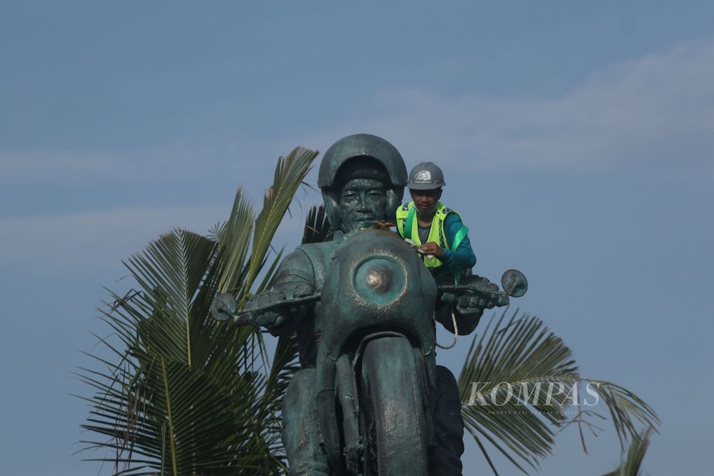 Pekerja membersihkan patung ”Speed” Jokowi karya seniman Nyoman Nuarta setelah dipasang di pintu gerbang hijau Sirkuit Mandalika, Lombok Tengah, Nusa Tenggara Barat, Minggu (13/3/2022). Patung seberat 3 ton dengan lapisan luar tembaga dan kuningan yang dioksidasi ini melambangkan kecepatan dan akselerasi yang dilakukan Presiden Joko Widodo. Patung kembali ditutup dengan kain hingga peresmian saat balapan MotoGP seri Indonesia, 18-20 Maret 2022.