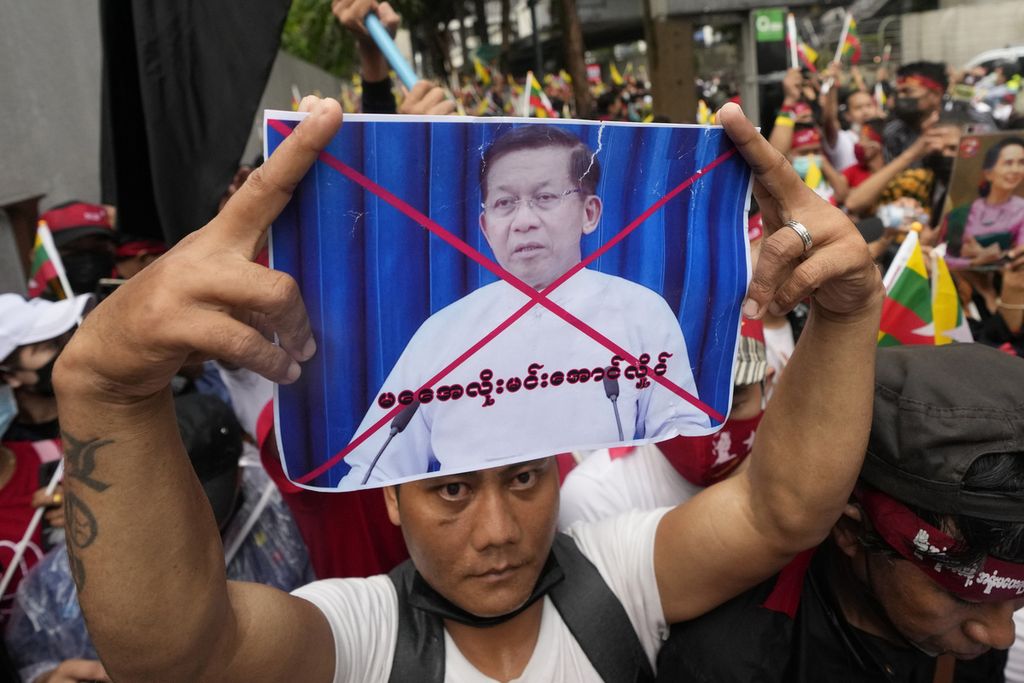 Seorang warga Myanmar yang tinggal di Thailand mengangkat poster foto pemimpin junta militer Myanmar, Jenderal Senior Min Aung Hlaing, dalam unjuk rasa di luar kantor Kedutaan Besar Myanmar untuk Thailand di Bangkok, Thailand, Selasa (26/7/2022). 