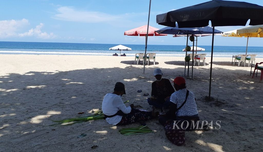 Tiga perempuan di Pantai Legian, Kuta, Badung, mengisi waktu sambil menunggu datangnya wisatawan ke tempat wisata andalan Bali, Sabtu (26/3/2022). Pandemi Covid-19 menghantam sendi-sendi ekonomi Bali, terutama kehidupan sektor pariwisata.