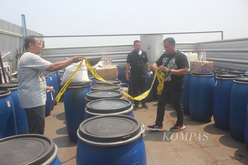Polisi memasang garis polisi pada 129 drum tempat pembuatan minuman keras ilegal di Jalan Jembatan Besi, Kecamatan Tambora, Jakarta Barat, Rabu (20/9/2023). Industri rumahan ini sudah beroperasi sekitar delapan bulan dengan omzet per bulan mencapai Rp 60 juta.