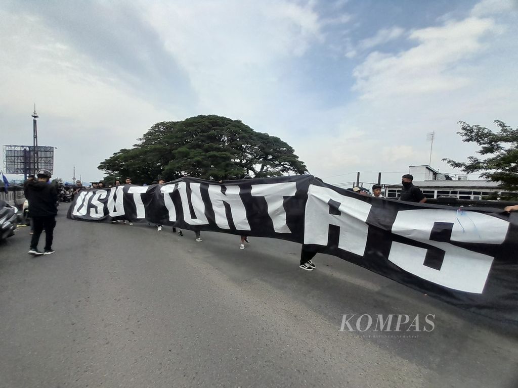 Spanduk besar bertuliskan ”Usut Tuntas” dibentangkan oleh kelompok suporter Arema FC, Aremania, saat menggelar aksi di atas <i>flyover</i> Arjosari, Kota Malang, Jawa Timur, Minggu (20/11/2022). 