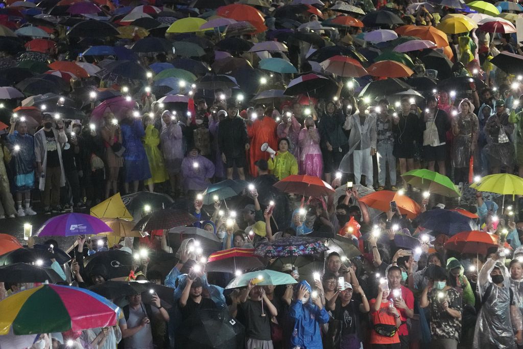 Di bawah guyuran hujan, ribuan pendukung Partai Bergerak Maju mengangkat telepon genggam ke atas dengan lampu kilat menyala saat berdemonstrasi di Bangkok, Minggu (23/7/2023). Mereka menyuarakan dukungannya terhadap MFP dan Pita Limjaroenrat yang dihadang oleh parlemen saat pemungutan suara PM Thailand.  