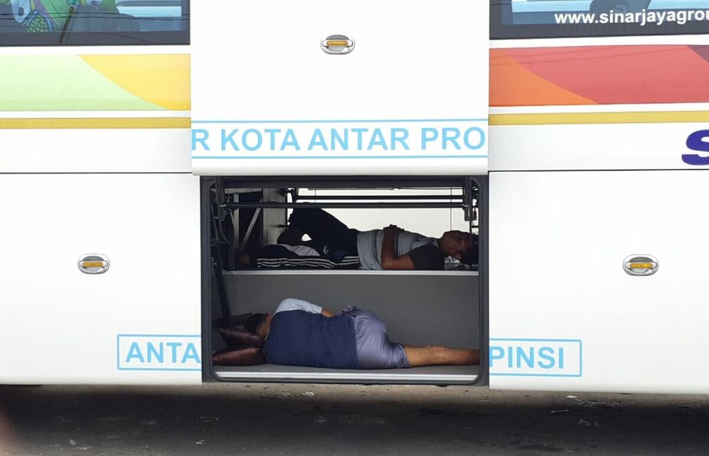Karyawan bus tidur di ruang bagasi bus yang terparkir di lapangan parkir bus Terminal Terpadu Merak, Cilegon, Banten, Rabu (28/4/2021).