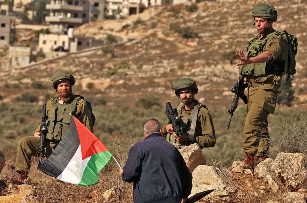 Seorang warga Palestina dengan memegang bendera Palestina berhadapan dengan aparat keamanan Israel dalam unjuk rasa di Beit Dajan, sisi timur wilayah pendudukan kota Nablus, Tepi Barat, 2 Desember 2022. Unjuk rasa itu untuk menentang pembangunan pos-pos luar Israel. 