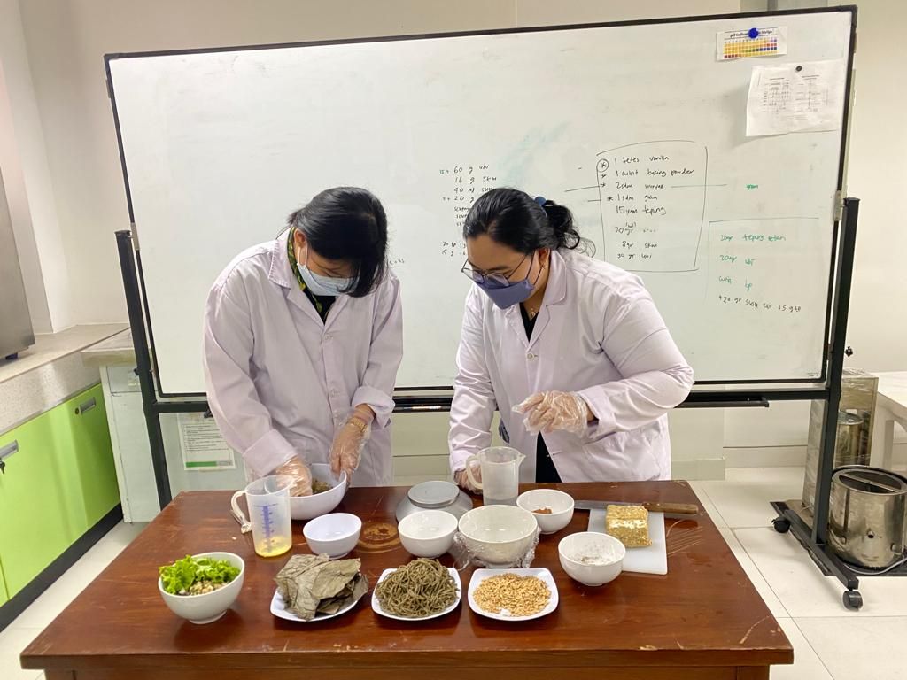 Victoria Diana Indah Lestari (kanan) dan, Audrey Layana Tjahyadi (kiri) saat berada di laboratorium Universitas Surabata di Jawa Timur pada Desember 2021. Mereka sedang mencoba membuat Mie Tebak, mie berprotein dari terigu, tempe dan daun sengkubak.