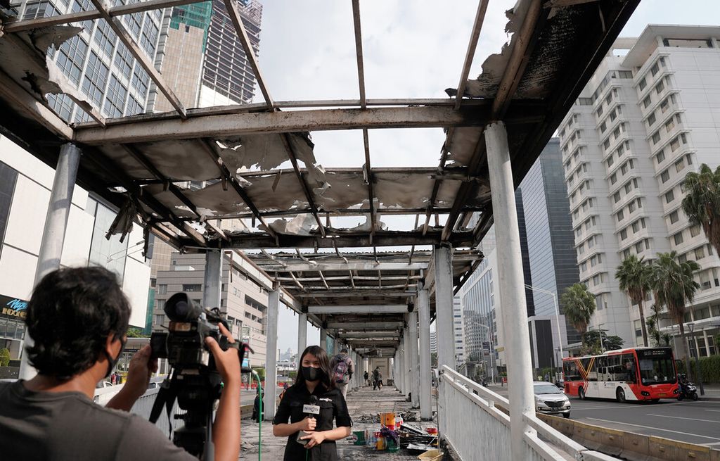 Jurnalis televisi melaporkan dari halte bus transjakarta Bundaran Hotel Indonesia yang dibakar massa pascademonstrasi di Jakarta Pusat, Jumat (9/10/2020). Unjuk rasa menolak Rancangan Undang-Undang Cipta Kerja yang diwarnai kerusuhan menyebabkan sejumlah fasilitas publik di Ibu Kota rusak.