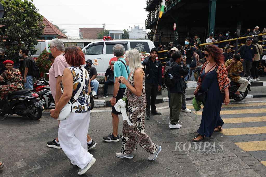 Wisatawan asing melintas di dekat pengunjuk rasa dari sejumlah elemen yang berkumpul sebelum menggelar aksi demonstrasi di Taman Parkir Abu Bakar Ali, Yogyakarta, tak jauh dari Stasiun Kereta Api Tugu, Yogyakarta, Kamis (22/8/2024). 