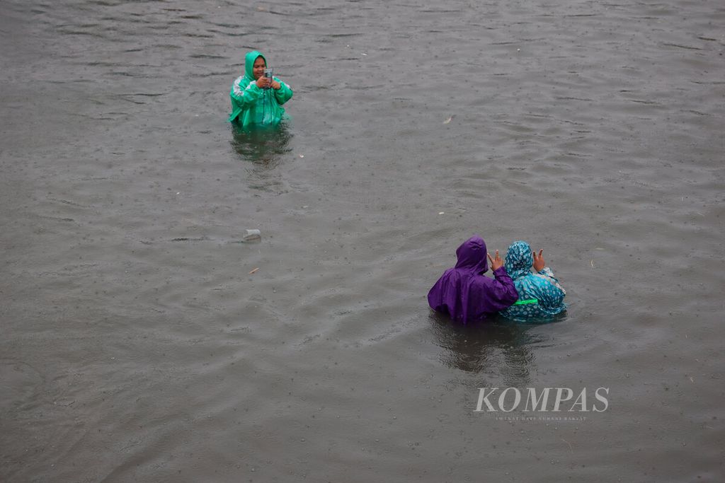 Warga berfoto di tengah genangan banjir yang terjadi di kawasan Kaligawe, Kota Semarang, Jawa Tengah, Sabtu (31/12/2022). 