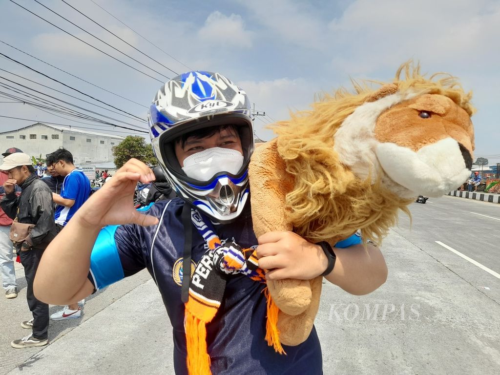Aremania menggendong boneka singa yang merupakan maskot dari Arema FC, Senin (18/7/2022), sesaat sebelum konvoi dalam rangka menyambut keberhasilan tim sepak bola asal Malang itu tiba usai merebut trofi Piala Presiden 2022.