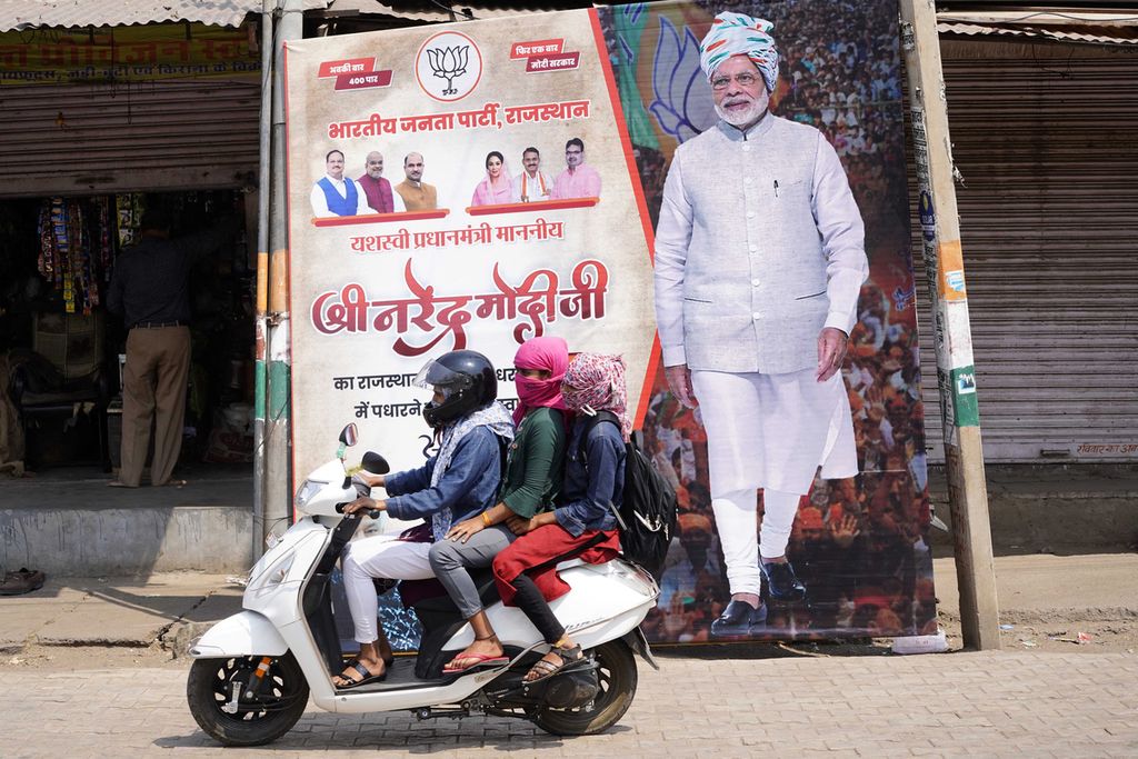 Pengendara sepeda motor melewati poster raksasa Perdana Menteri India Narendra Modi di Dausa, India, 12 April 2024. 