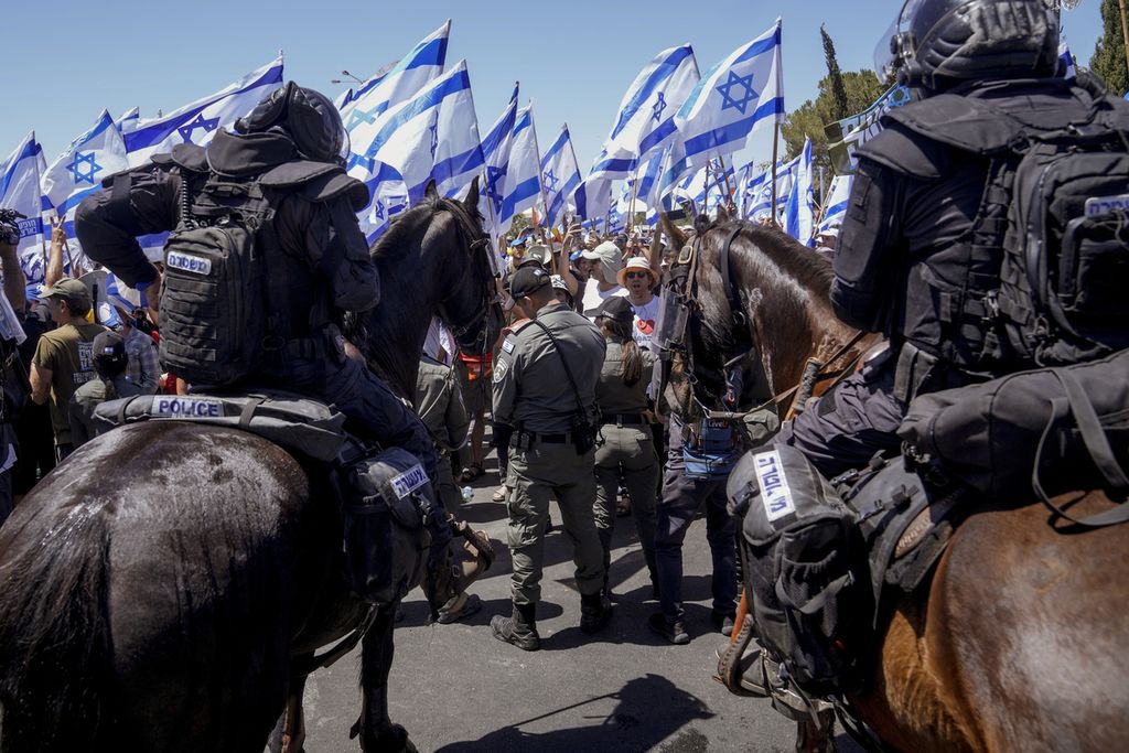 Para pengunjuk rasa membentangkan bendera Israel saat berhadapan dengan pasukan keamanan berkuda di Jerusalem, Senin (24/7/2023), pascapengesahan UU Reformasi Hukum oleh parlemen.