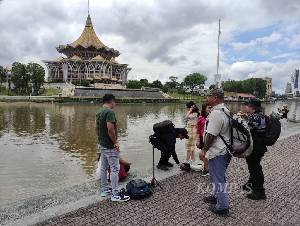 Sejumlah wisatawan bercengkerama di tepi Sungai Sarawak dengan latar gedung parlemen atau Dewan Undangan Negeri Sarawak di Kuching, Malaysia, Kamis (27/6/2024).