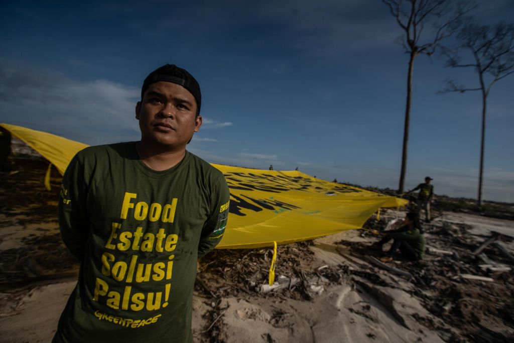 An environmental activist pulls up a large banner that reads "Food Estate Feeding Climate Crisis" in the cassava food estate area in Tewai Baru Village, Gunung Mas Regency, Central Kalimantan, Thursday (10/11/2022).