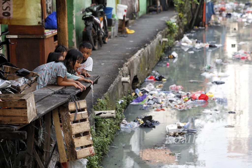Anak-anak bemain di tepian terusan Sungai Krukut di kawasan permukiman padat penduduk Kebon Kacang, Jakarta Pusat, Selasa (30/5/2022). Pemerintah akan mengevaluasi standar garis kemiskinan di Indonesia agar pengentasan kemiskinan bisa menyasar lebih banyak masyarakat rentan.