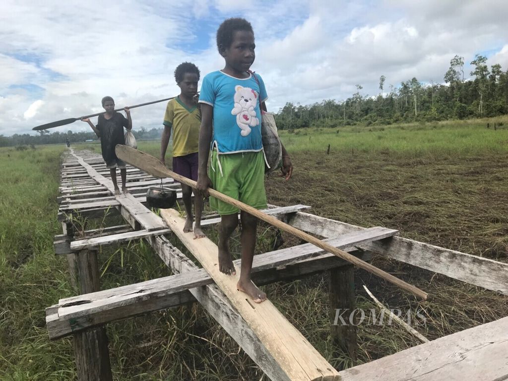 Anak-anak dari Kampung Somnak, Distrik Joutu, Kabupaten Asmat, Papua, menyusuri jalan-jalan di atas papan untuk menuju perkampungan, Rabu (14/8/2019). Kampung di pedalaman Asmat ini dikelilingi rawa-rawa yang luas. 
