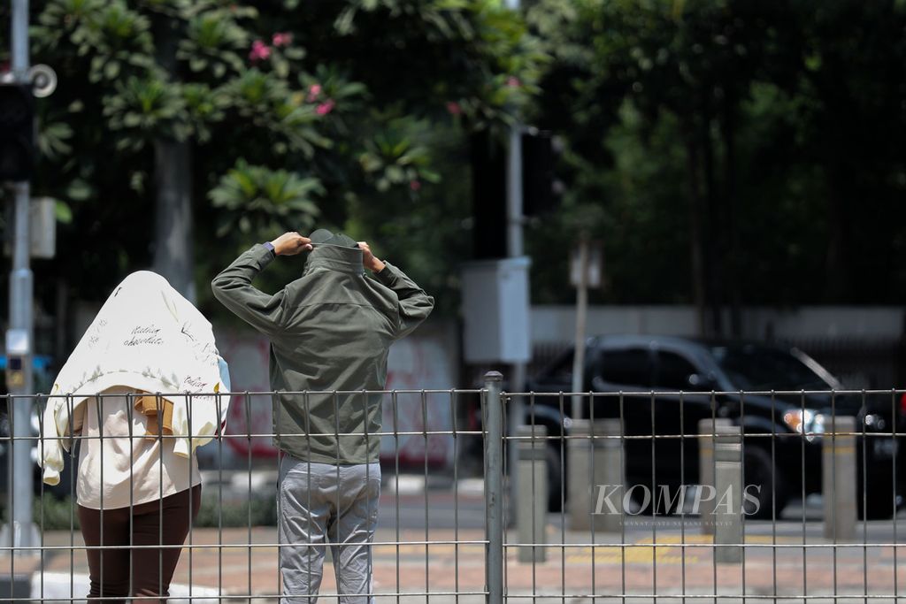Warga menggunakan jaket untuk melindungi kepala dari terik matahari di kawasan Jalan Sudirman, Jakarta, Senin (9/10/2023). Suhu panas yang terjadi akhir-akhir ini berlanjut hingga November 2023. 