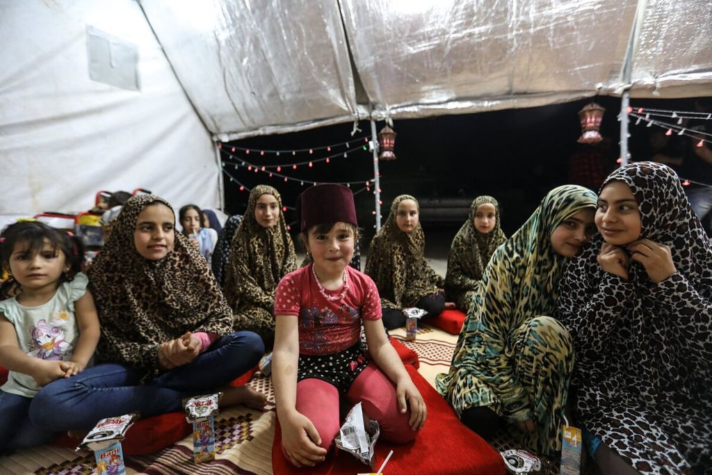 Ekspresi anak-anak yatim piatu yang menjadi korban selama perang saudara di Suriah saat mereka mendengarkan dongeng tradisional pada bulan Ramadhan di tenda pengungsi kamp Al-Aramel di pinggiran kota Dana, perbatasan Turki-Suriah.
