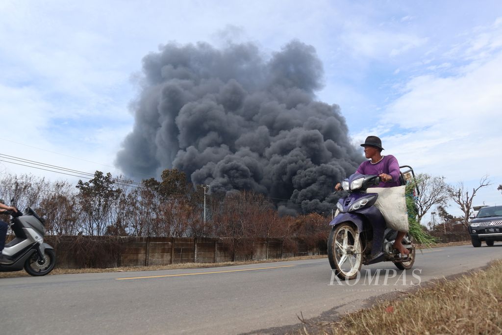 Warga melintas di depan kobaran api yang melanda kawasan PT Pertamina RU VI Balongan, Kabupaten Indramayu, Jawa Barat, pada 30 Maret 2021.