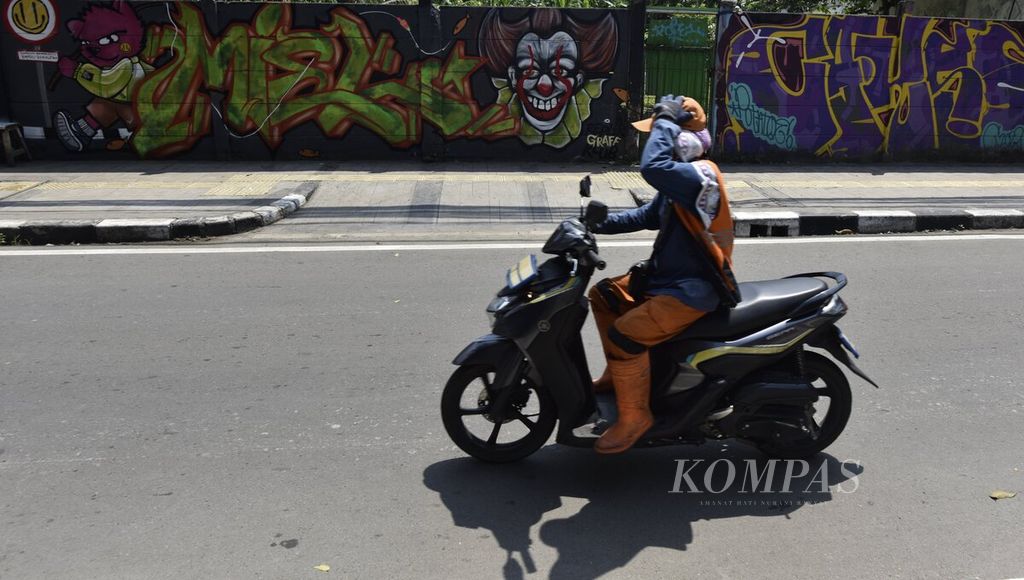 Pengendara sepeda motor memegang penutup kepala saat melintas di Jalan Jaksa, Jakarta Pusat, saat siang hari, Senin (24/4/2023). 
